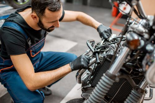 A man in a repair shop is performing regular motorcycle maintenance.