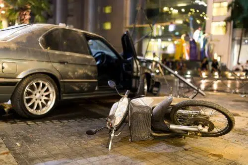 A car door is open and a motorcycle is lying in the street after a serious car accident.