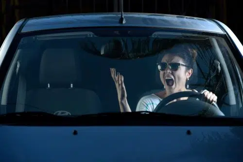 A woman with road rage gesturies angrily in her car.