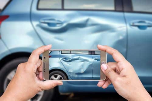A person takes a photo of damage after a car accident in a rental car.