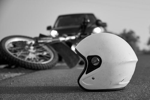 A black and white photo signifying a fatal motorcycle accident. A car is parked next to a helmet and overturned motorcycle.