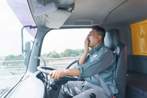 A fatigued truck driver behind the wheel of his truck.