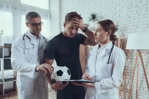 Two doctors tend to a patient with a concussion brain injury after a sports injury.