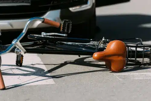 A closeup of a bicycle laying in front of a car after being struck in an accident.