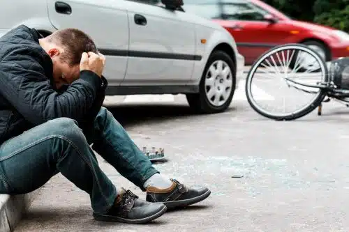 A distraught man sits on the sidewalk after a pedestrian accident.
