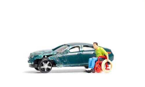 Two plastic models, side by side, one of a destroyed, green car, and the other of a man in a wheelchair.