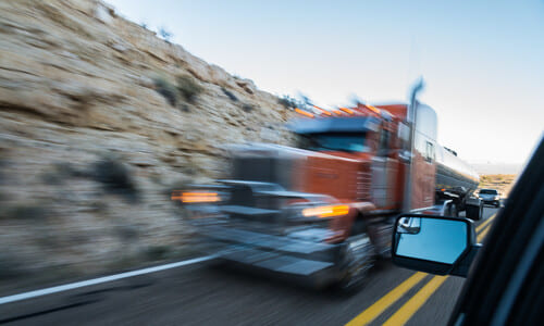 A motion-blurred, red semi truck seen from a driver's perspective through their car window.