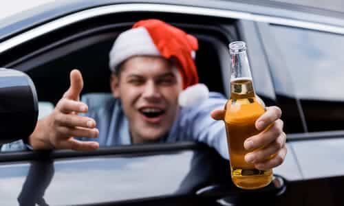 A blurred out, drunk, smiling teenager in a santa hat, leaning out from the driver's seat with a bottle of bear in hand.