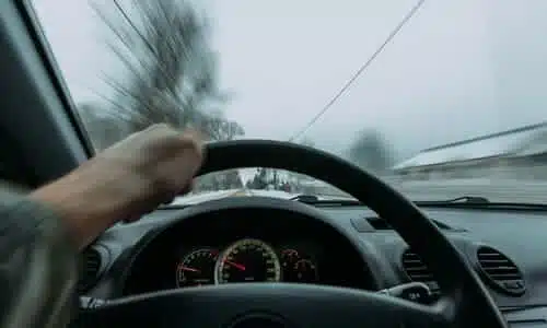 A blurry, first-person shot of a driver behind the wheel of his car, speeding while over the road's center line.