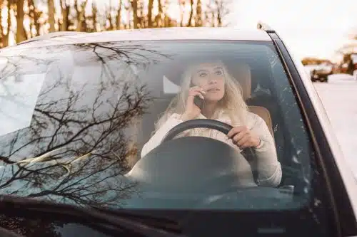 A blonde middle aged woman talks on the phone, distracted while driving her car.