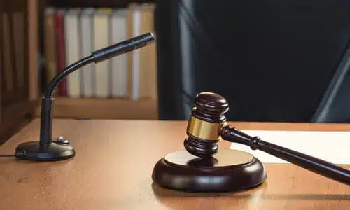 A gavel and soundblock on a judge's bench, next to a microphone, with a black chair in the background.