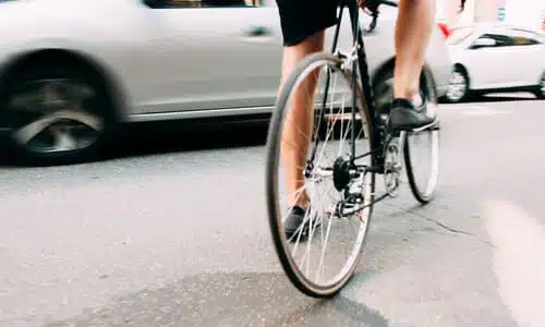 A bicyclist approaching a motion-blurred grey sedan from the side, about to be involved in an accident.