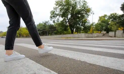 A pedestrian in black jeans and white shoes about to cross the road on a crosswalk.