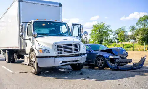 A collision between a large, white truck and a smaller vehicle on a suburban road.