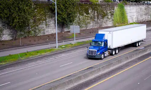 A blue semi truck pulling a trailer behind it as it speeds down a highway.