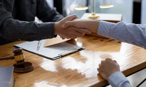 A client and his defective product lawyer shaking hands at a desk to begin working together.