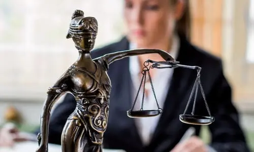 A selective focus shot of a Lady Justice desk statue with a working medical malpractice lawyer in the background.