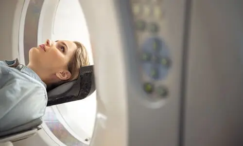 A woman in a hospital gown lying down and about to enter a CT scanner.